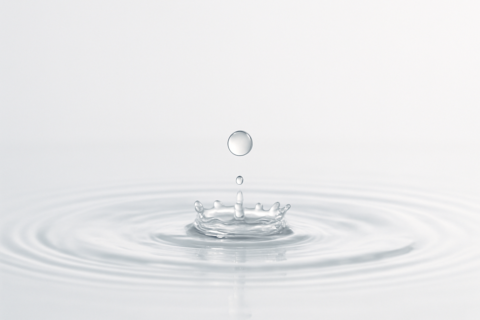 Very low key background. Mostly white background, with a droplet hitting a pool of clear liquid